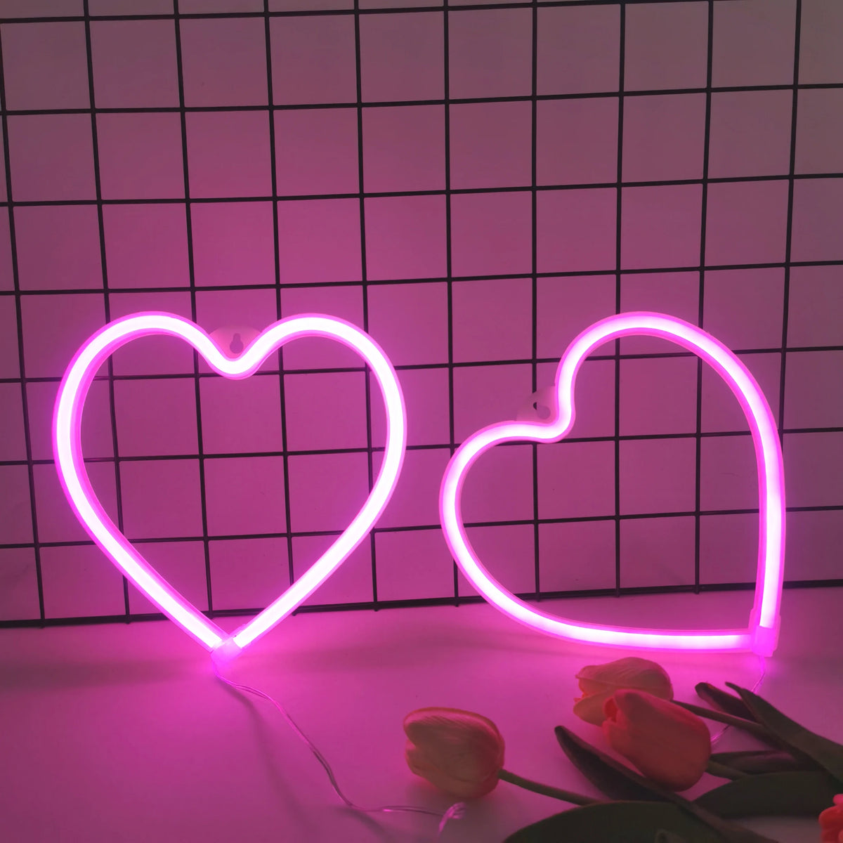 Two neon heart signs glow pink on a grid background with roses in the foreground.