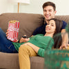 A smiling couple relaxing on a couch, with a woman holding a red popcorn bag.