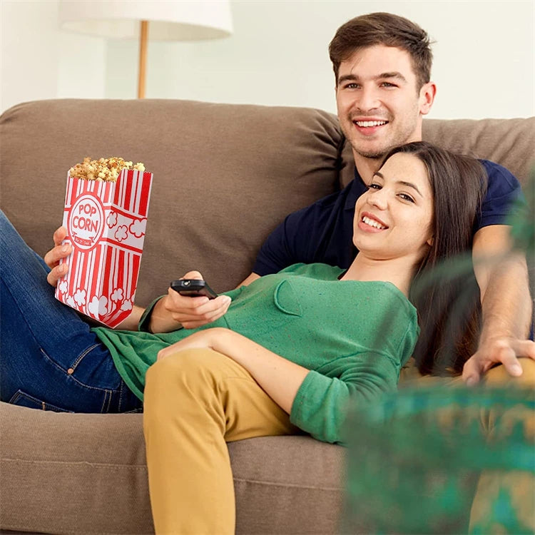 A smiling couple relaxing on a couch, with a woman holding a red popcorn bag.