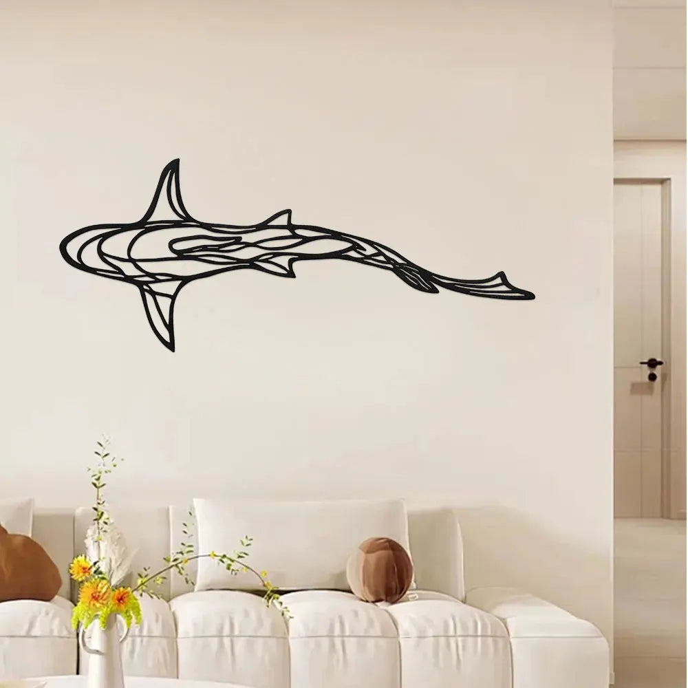 Black metal line sculpture of a shark swimming horizontally on a white wall above a sofa.