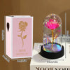 A pink box containing an eternal rose in a glass dome with a glowing stem and leaves.