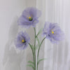 A large artificial silk purple poppy flower with a green stand displayed against a white wall.