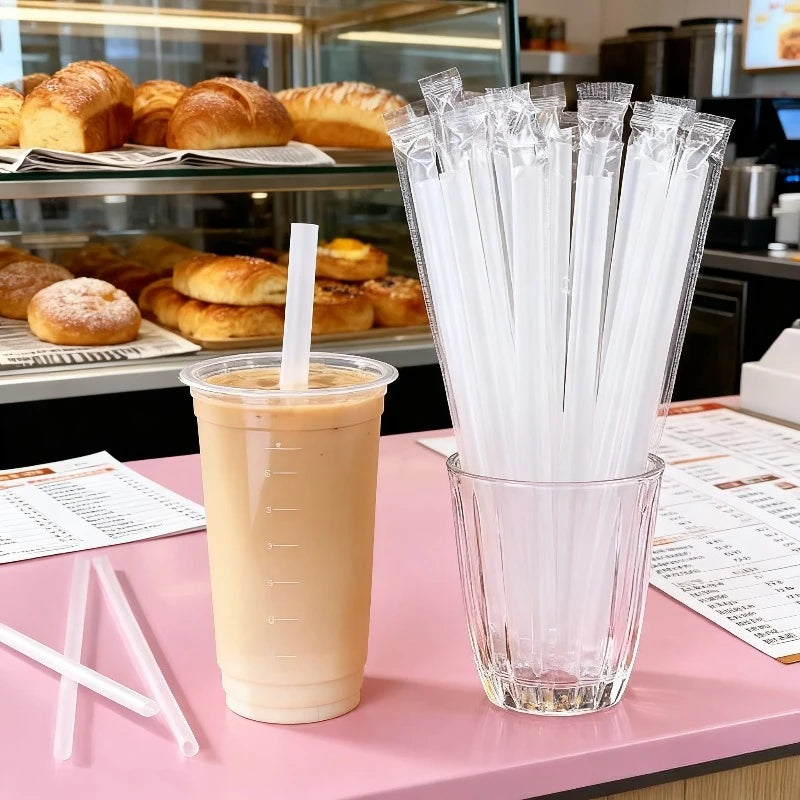 A glass jar filled with clear plastic drinking straws is displayed next to a glass of light orange beverage.