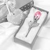 A silver crystal rose artificial flower resting in a white velvet box with a heart-shaped tag and ribbon.