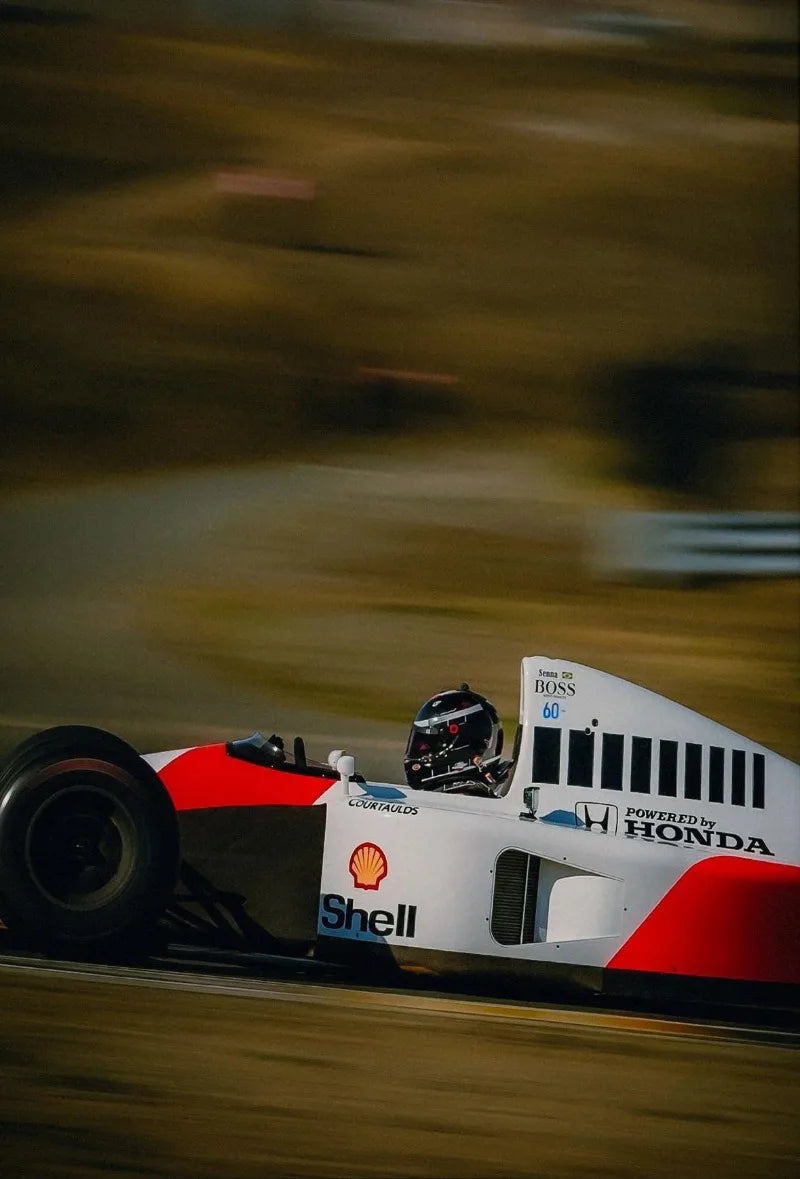 A blurred shot of a race car speeding along a track, featuring red and white livery with Shell and Honda branding.