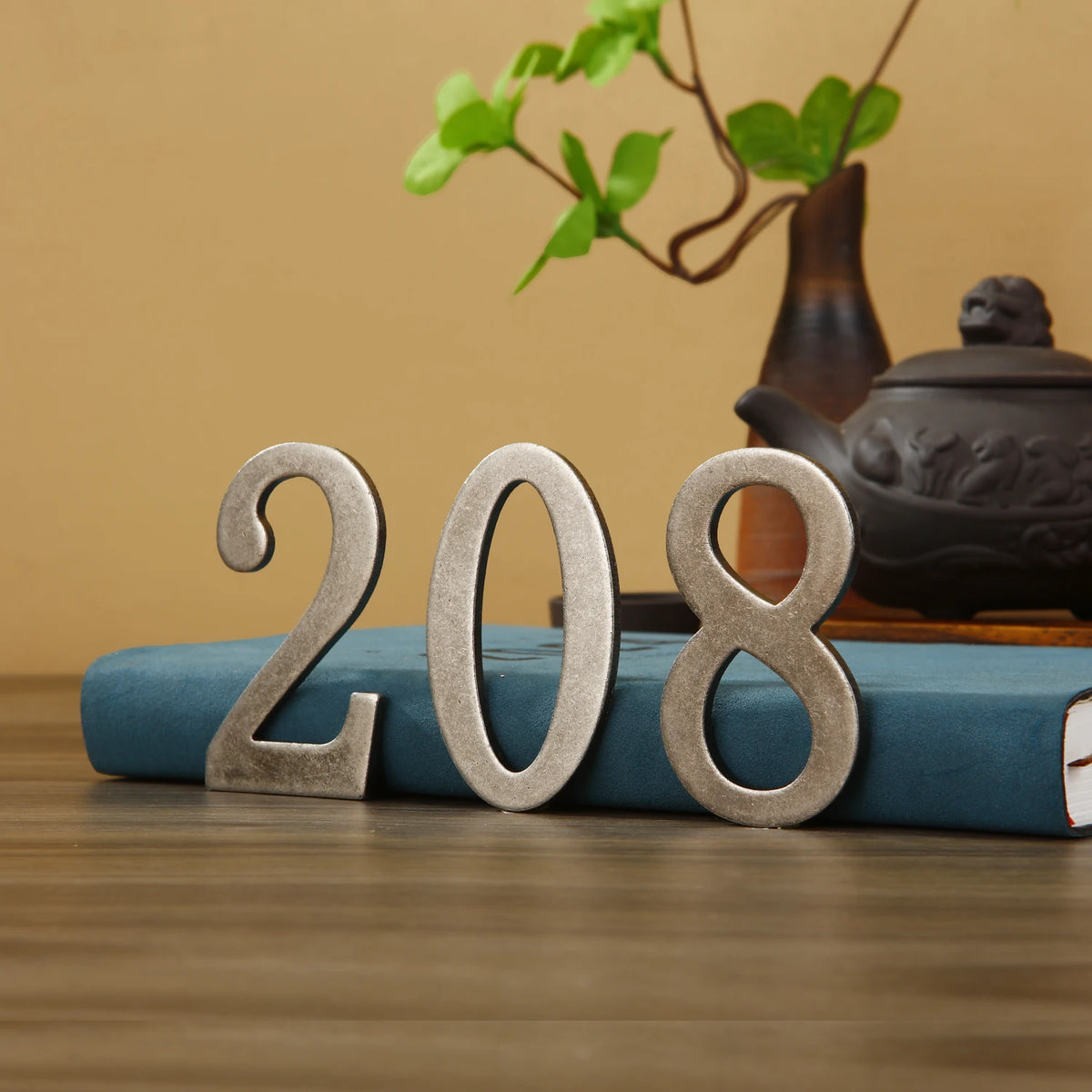 Magnetic silver house number for doors and mailboxes with the year 208 on a blue book.