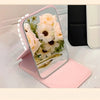 A pink portable folding HD makeup mirror with a floral design resting on a white surface.