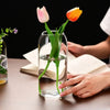 A clear glass vase holds two pink and orange tulips on a wooden table.