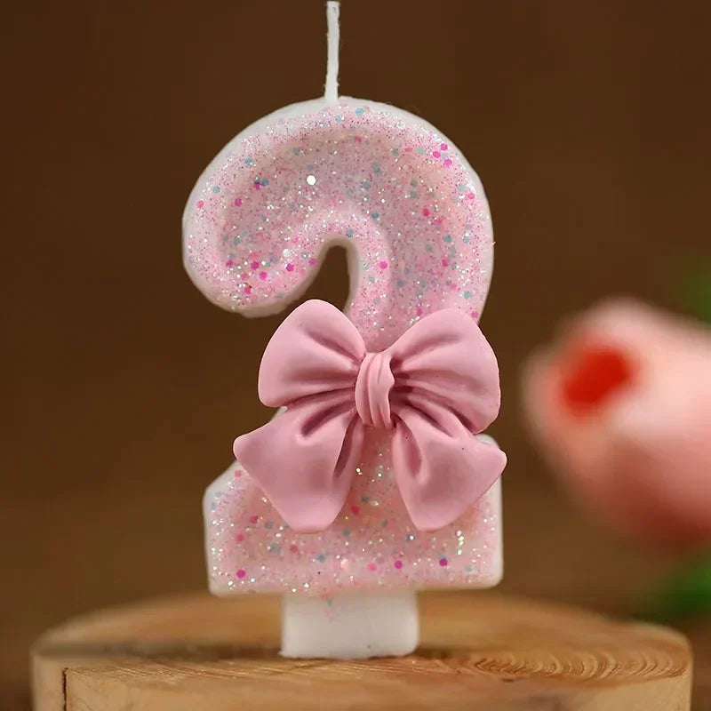 A pink glitter number candle shaped like the digit 9 with a pink bow on a wooden surface.