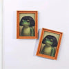 Two framed photos of a green frog head in natural wood frames