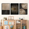 A set of three abstract canvas prints featuring concentric circle patterns in gold and black tones mounted on a wooden shelf.