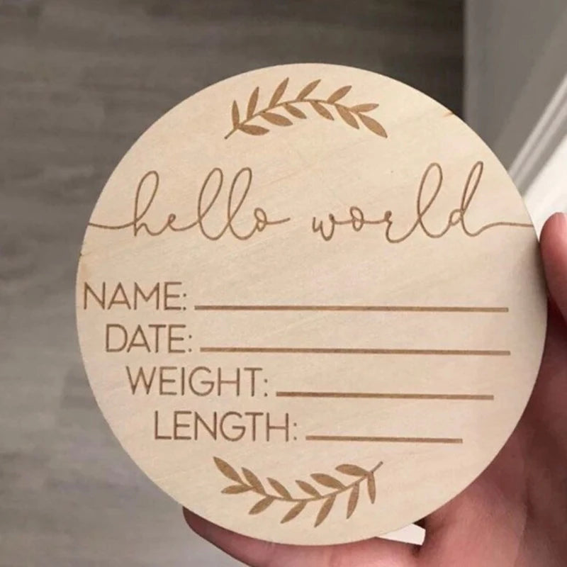 A round wooden sign for a newborn keepsake with lines for name, date, weight, and length, surrounded by a laurel wreath desig