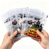 A hand holds a stack of clear self-adhesive treat bags decorated with Halloween graphics and pumpkins.