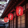 A cluster of red Japanese paper hanging lanterns with white cherry blossoms are displayed under a traditional roof structure.
