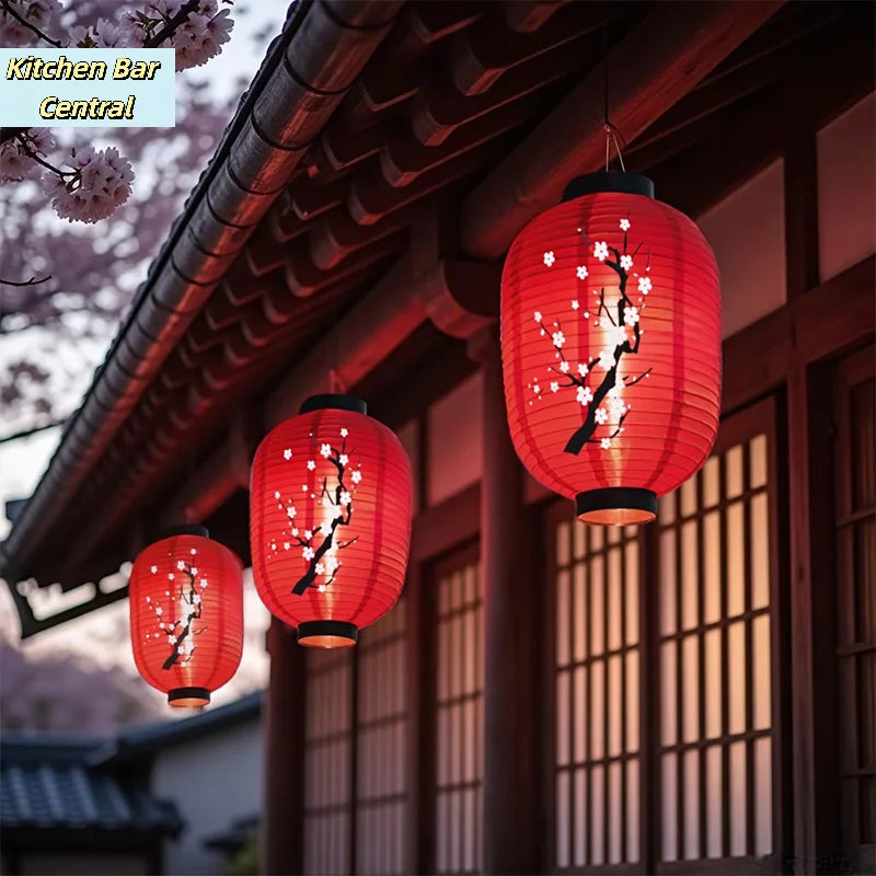 A cluster of red Japanese paper hanging lanterns with white cherry blossoms are displayed under a traditional roof structure.
