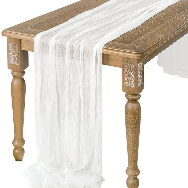 A semi-sheer white gauze table runner draped over a wooden table.