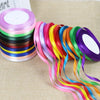 A collection of colorful satin ribbon spools in various shades of pink, green, blue, and yellow laid out on a beige surface.
