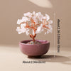 A handcrafted crystal tree featuring white quartz flowers on a copper wire base, set in a pink bowl.