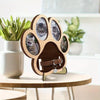 A wooden paw print frame with four photo cutouts for a pet memorial displayed on a light wood table.
