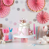 A tiered pink and gold cake decorated with pearl accents, surrounded by pink and silver party decorations.