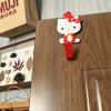 A white and red cartoon cat hook is displayed on a wooden surface.