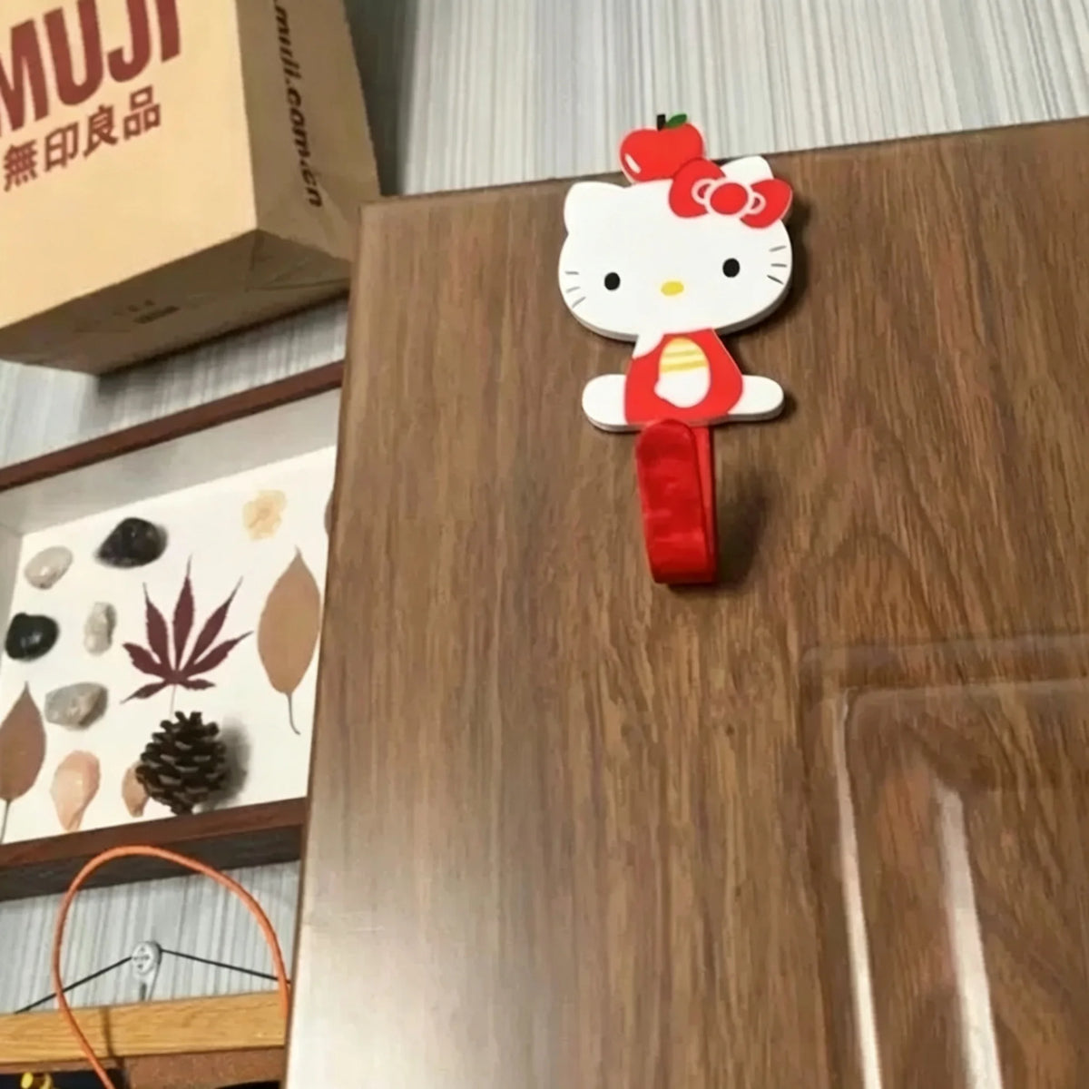 A white and red cartoon cat hook is displayed on a wooden surface.