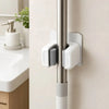 A close-up of a silver wall holder with three white adhesive grips for storing mops, brooms, and long-handled tools.