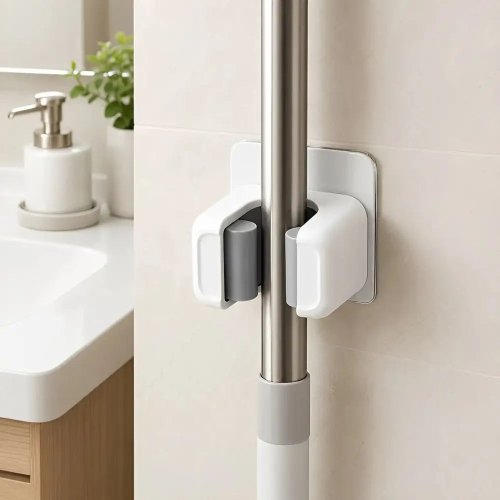 A close-up of a silver wall holder with three white adhesive grips for storing mops, brooms, and long-handled tools.