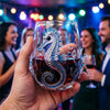 A hand holds a blue-ringed octopus stemless wine glass filled with red liquid, decorated with handcrafted ocean theme.