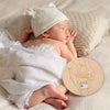 A newborn baby sleeping peacefully on a soft blanket with a knitted hat and a wooden handprint keepsake sign.
