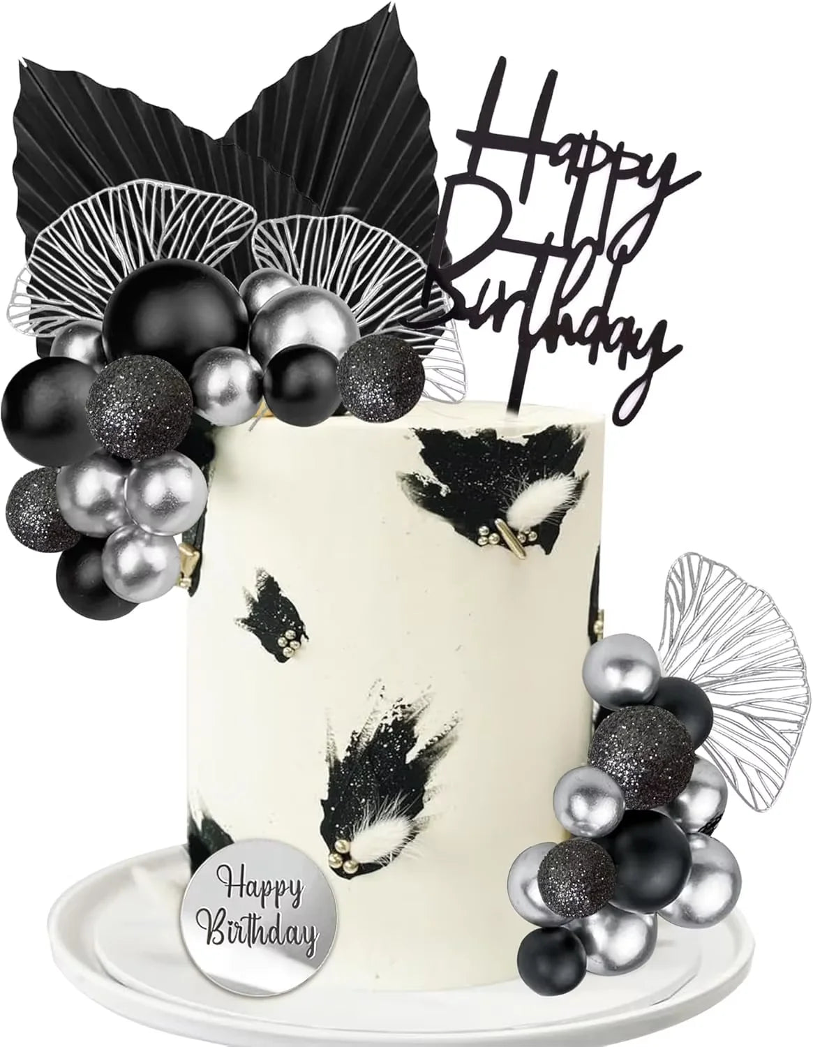 A white cake decorated with black and silver feathers and gold accents, topped with a black birthday banner and surrounded by