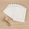 A set of white kraft paper photo display frames and wooden clips are arranged on a light wood surface.
