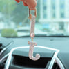 A hand holds a crystal letter keychain charm shaped like the letter J against a blurred background of a car interior.