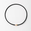 A black string bracelet with a gold plated clasp laid flat on a white background.