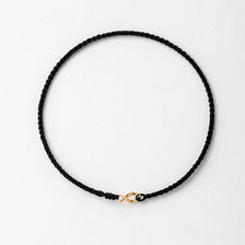 A black string bracelet with a gold plated clasp laid flat on a white background.