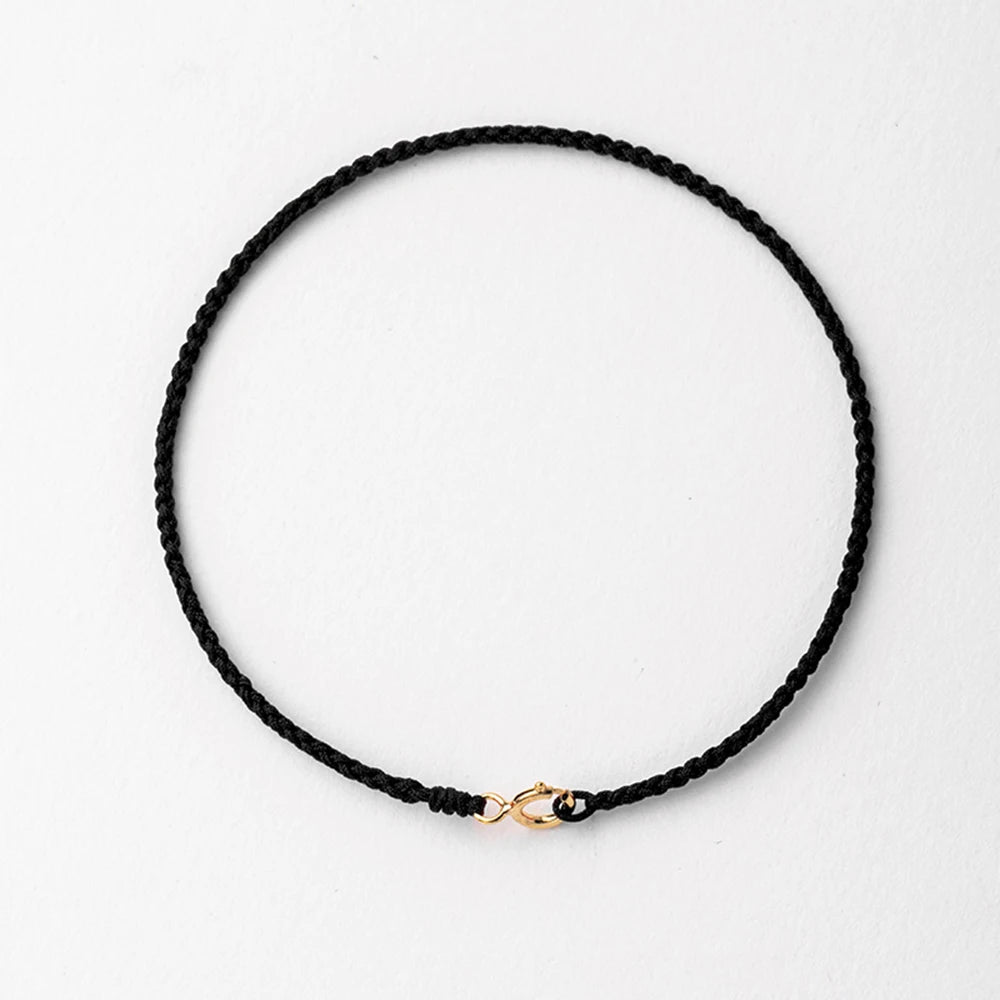 A black string bracelet with a gold plated clasp laid flat on a white background.