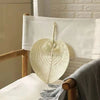 A light beige peach-shaped hand fan woven from bamboo fibers resting on a white linen cloth.