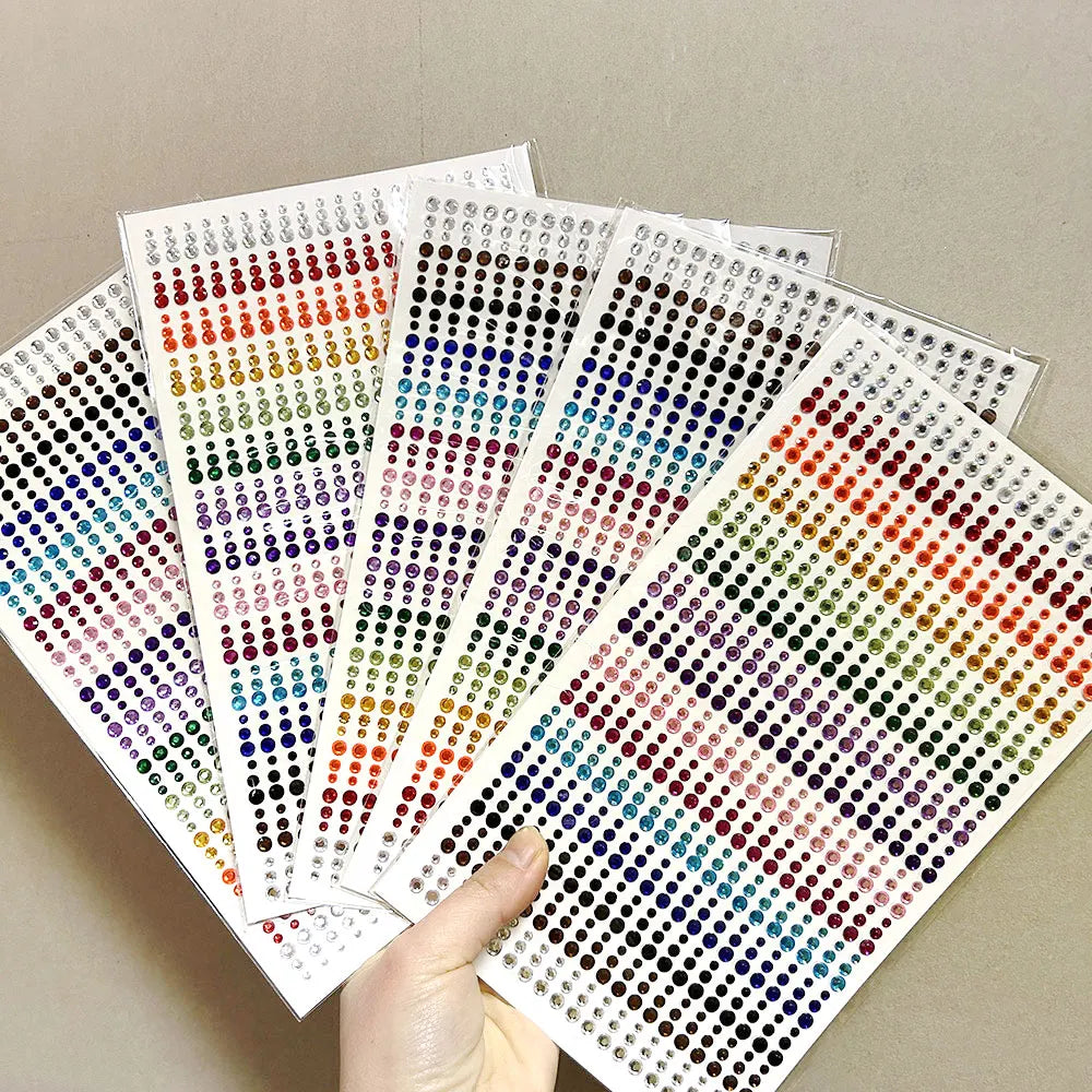 A hand holds several sheets of glitter gem stick-on facial tattoos displaying a wide variety of colorful gems.