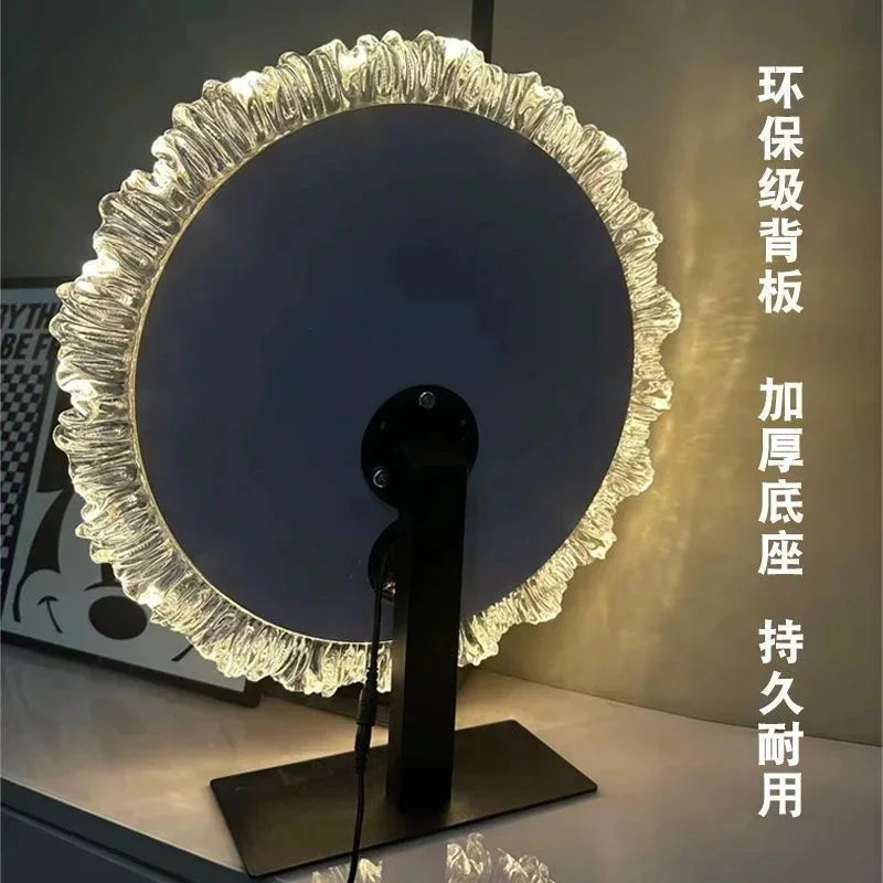 A round, textured glass vanity mirror with an illuminated frame and a black stand.