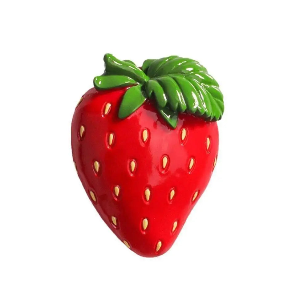 A bright red strawberry with a green leafy top, used as a fridge magnet.