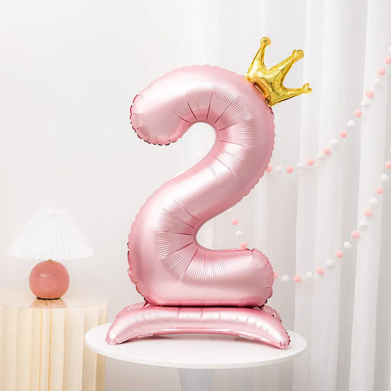 A pink foil balloon shaped like the number two with a gold crown on top