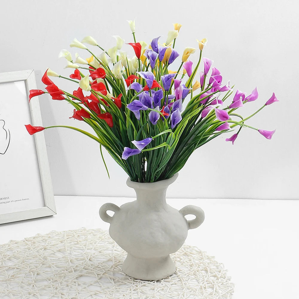 A vibrant bouquet of artificial calla lilies in red, purple, and yellow hues displayed in a gray vase.
