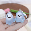 A light blue glow-in-the-dark ghost keychain is held in a hand against a blurred background.