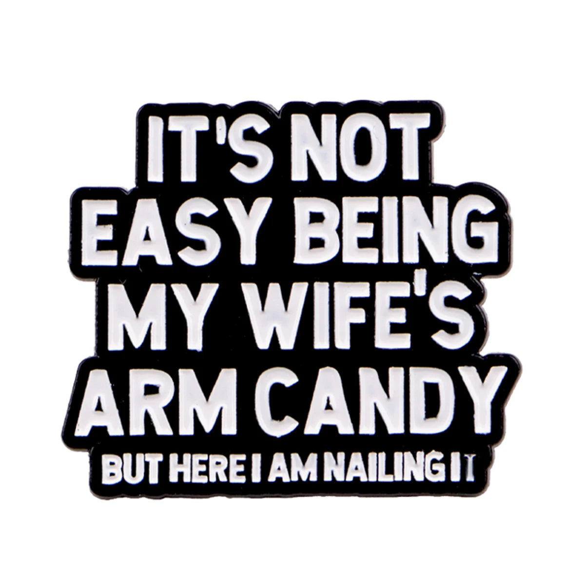 Black enamel pin with white text that reads It's not easy being my wife's arm candy but here I am nailing it