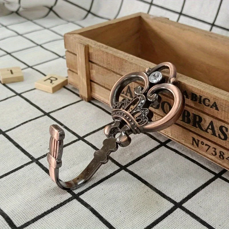 A pair of vintage crown curtain hooks with silver and bronze accents resting on a wooden box.