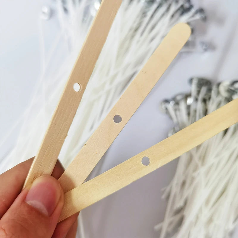 Three wooden candle wicks are held by a hand against a background of white fibers.