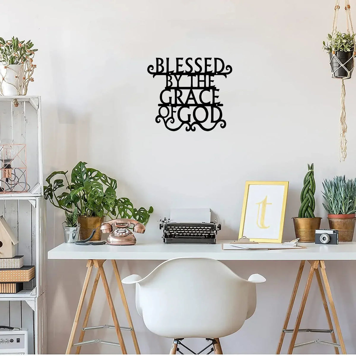Black metal wall art sign with the text Blessed by The Grace of God displayed on a white desk.