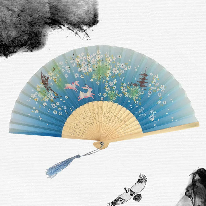 A vintage bamboo folding hand fan with light blue and white floral patterns is shown against a white background.