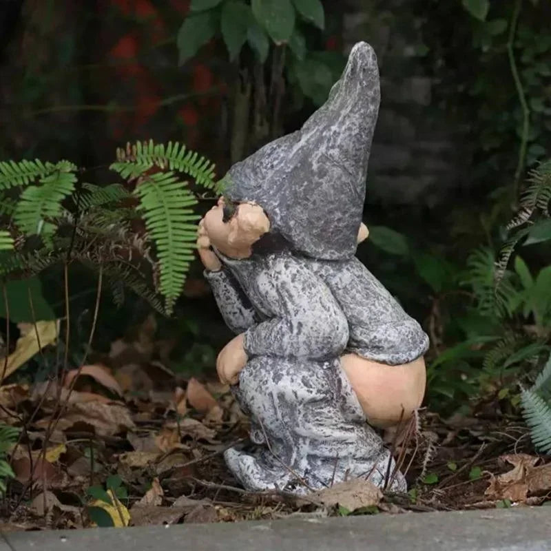 A gray gnome statue with a pointed hat is nestled in a natural garden setting.