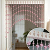 Rideau de porte en perles de cristal artificiel rose avec arc festonné, suspendu dans un cadre de porte blanc.